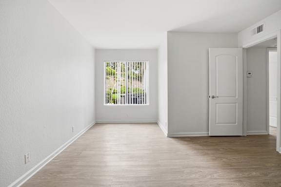 A room with a white door and a window with a view of trees.