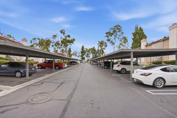 A street view with cars parked on both sides and a white car in the foreground.