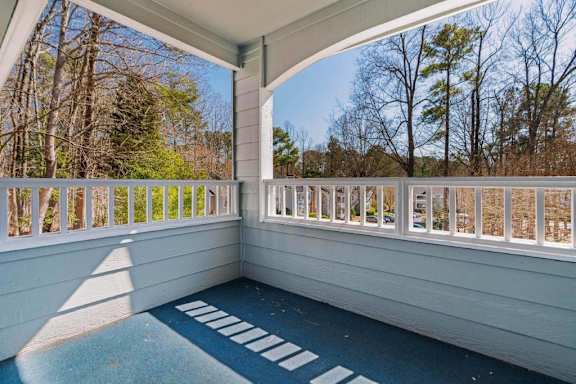 A sunny day on a white balcony with a view of trees.