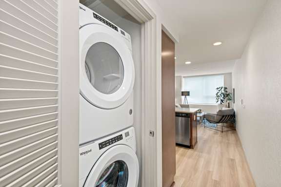 A white washing machine is in a small room with a wooden floor.