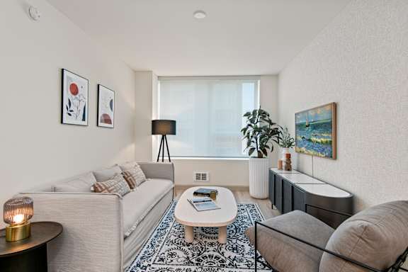 A living room with a grey couch, a white coffee table, and a large window.