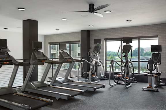 A gym with treadmills, elliptical machines, and a fan.