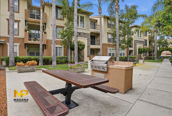 A park area with a picnic table and bench in front of apartment buildings.
