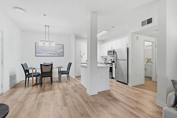 A dining room with a table set for four and a kitchen in the background.