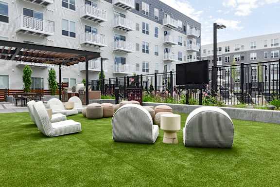 A white and grey building with a black fence and a green lawn with white chairs and tables.