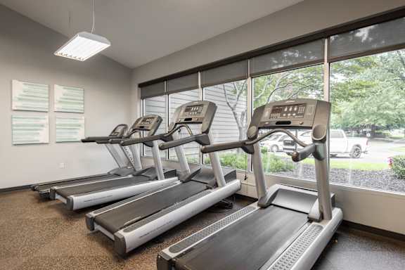 A gym with treadmills and a car visible through the window.