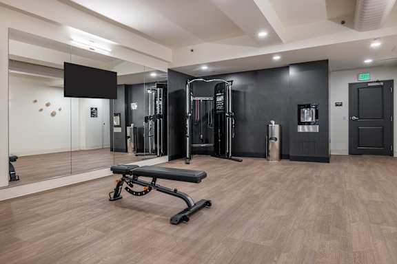 A gym with a bench, weights, and mirrors.