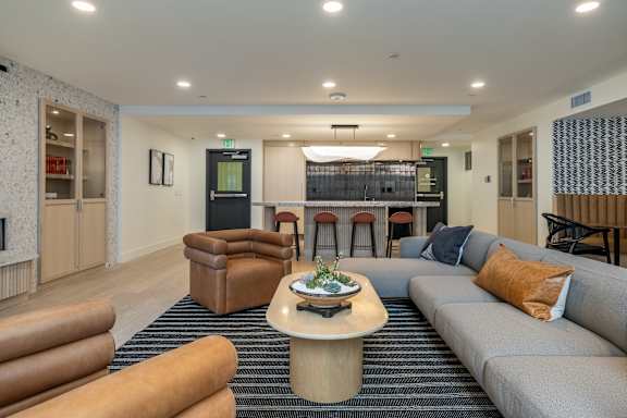 A modern living room with a grey sofa, a wooden coffee table, and a bar area in the background.