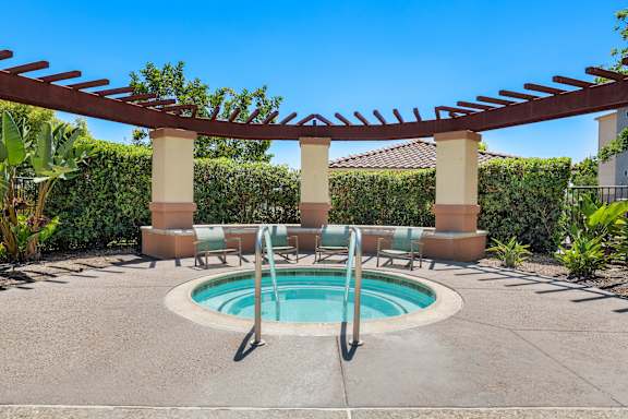 A pool surrounded by a concrete patio and a pergola.