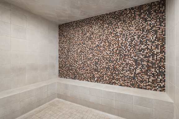 A bathroom with a brown tile wall and white tiled floor.