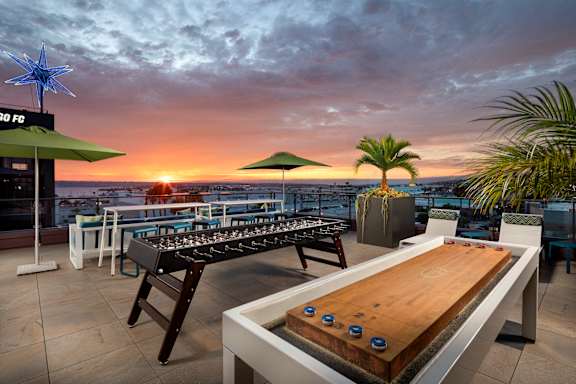 A shuffleboard table is in the foreground of a sunset scene.