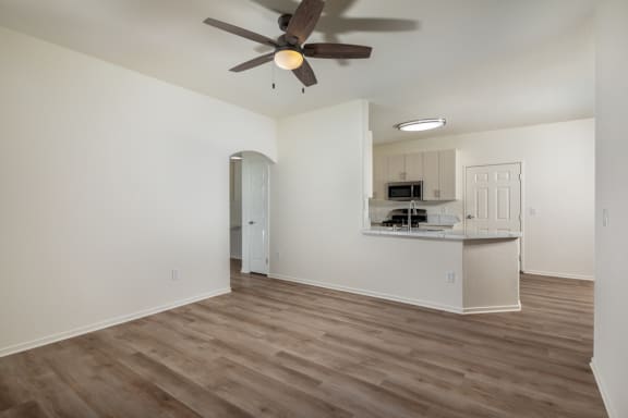 an empty living room with a ceiling fan and a kitchen