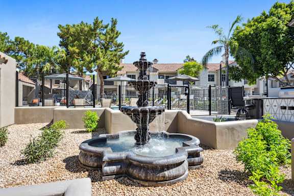 A fountain in the middle of a garden with houses in the background.