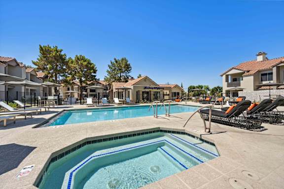A large outdoor swimming pool surrounded by lounge chairs and buildings.
