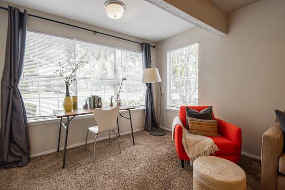 A room with a red chair and a table with a lamp on it.