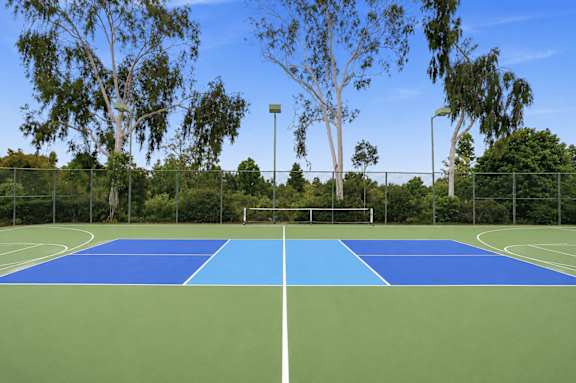 A tennis court with a blue top and green bottom is surrounded by trees.