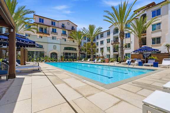 A large swimming pool surrounded by lounge chairs and umbrellas in front of a hotel.