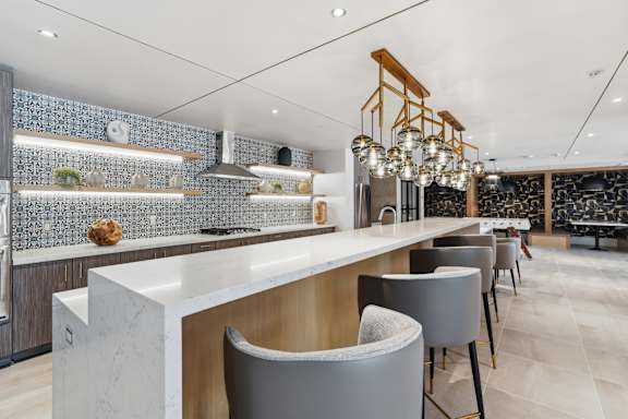 A modern kitchen with a long white island and grey chairs.