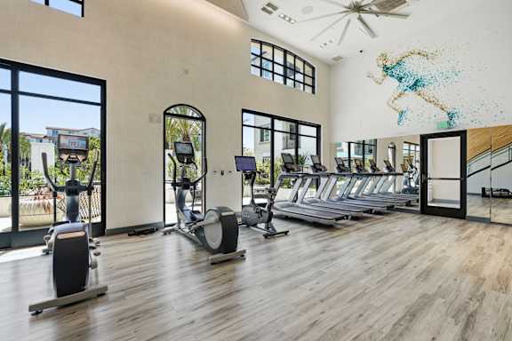 A gym with a row of treadmills and elliptical machines.