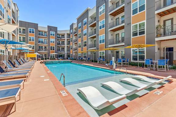 A swimming pool surrounded by sun loungers and apartment buildings.