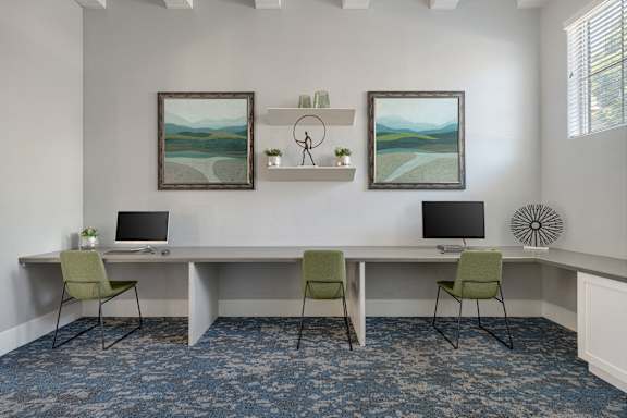 A room with a desk, chairs, and two paintings on the wall.