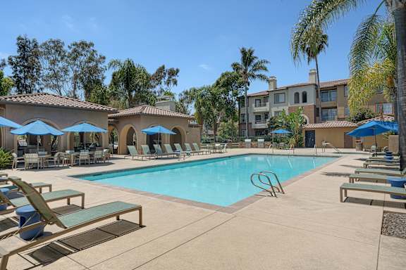 A swimming pool surrounded by sun loungers and umbrellas.