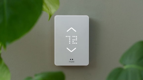 a white indirect thermostat sitting on a wall next to a green plant
