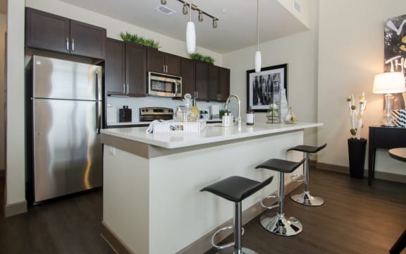 a kitchen with a large island with stools and a stainless steel refrigerator