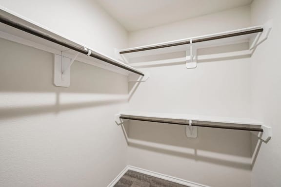 a spacious walk in closet with a white wall and a hanging rack