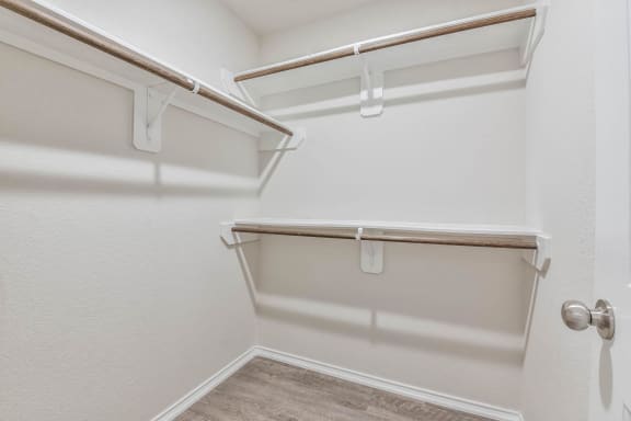 a walk in closet with a white wall and a shelf on the wall