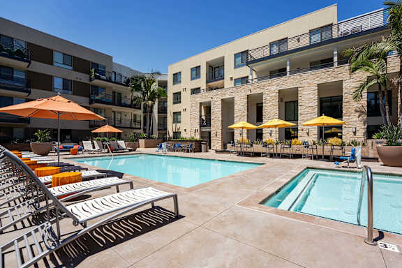 A pool area with sun loungers and umbrellas in front of a building.