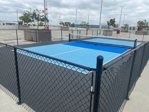 A blue tennis court is surrounded by a black fence.
