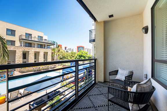 A balcony with a chair and a table overlooking a pool.