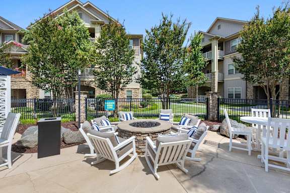 A patio with chairs and a fire pit in front of apartment buildings.