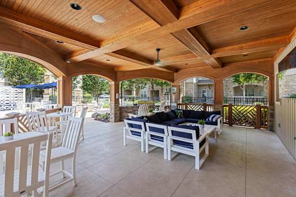 A wooden patio with white chairs and a black couch.