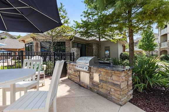 A patio with a grill and chairs under an umbrella.