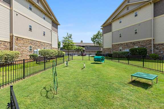 A black fence surrounds a green lawn with a tennis court and a bench.