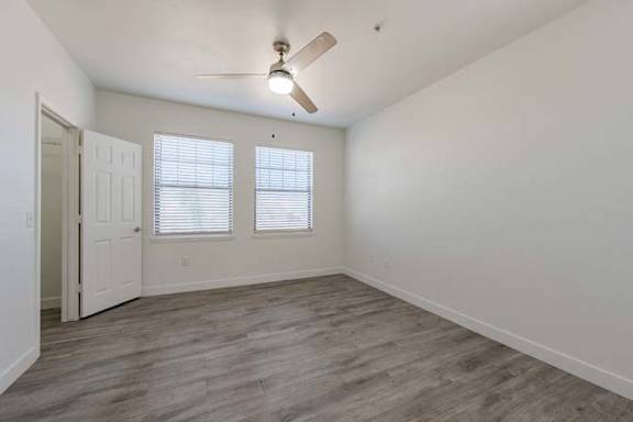 A room with a ceiling fan and two windows.
