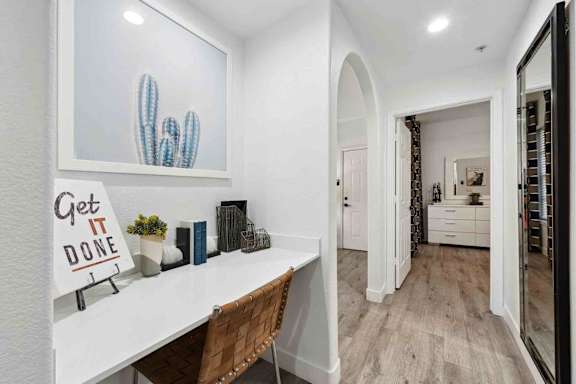 A white desk with a sign that says "Get it Done" sits in a room with a cactus and a mirror.