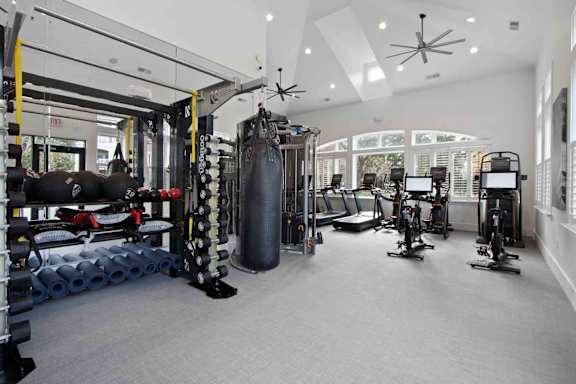 A spacious gym with a variety of equipment including a treadmill, a stationary bike, a rowing machine, a punching bag, and a bench press.