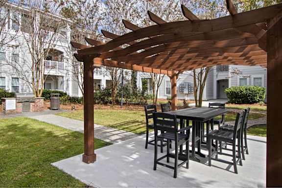 A wooden pergola is over a table and chairs.