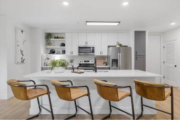 A modern kitchen with a white island and two chairs.