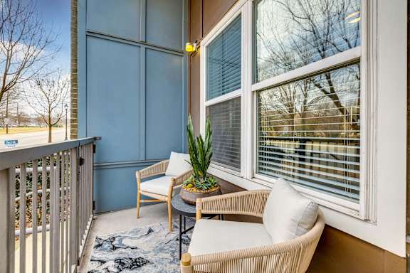 A balcony with a table, chairs, and a potted plant.