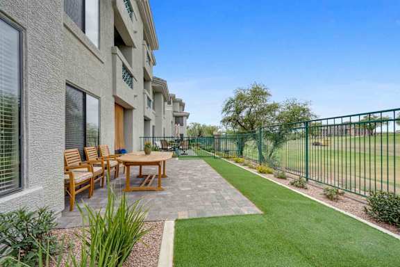 A patio with a table and chairs is surrounded by a green fence.