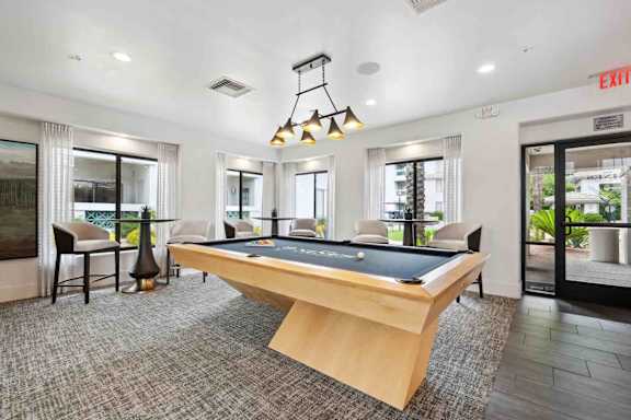 A pool table is in the middle of a room with a chair and a lamp.