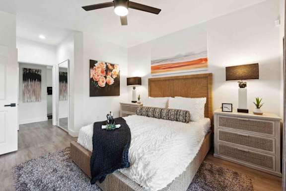 A bedroom with a large bed, a ceiling fan, and a painting on the wall.