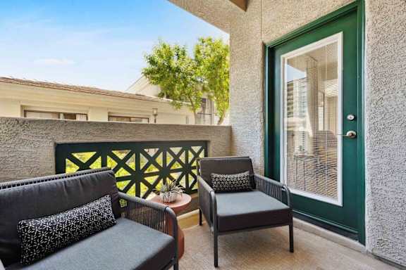 A balcony with a black couch and a small table with a plant on it.