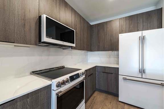 A kitchen with a white fridge, white countertop, and a black microwave.