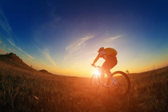 A person riding a bicycle in a field during sunset.