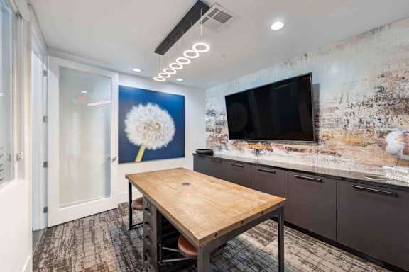 A room with a wooden table and a television on the wall.